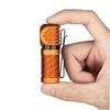 Hand holding an orange Olight S1R Baton II flashlight with a black pocket clip, demonstrating its compact size.