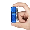 Hand holding small blue Olight flashlight with black pocket clip, white background.