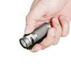 Hand holding a grey Olight compact flashlight with textured body and black clip, pressing the side button.