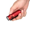 Hand holding a compact red Olight flashlight featuring textured grip and pocket clip against a white background