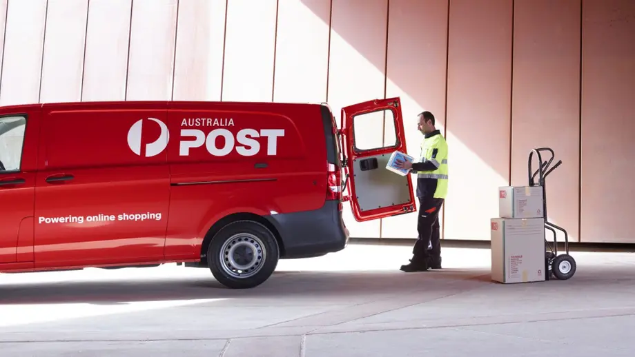 Red Australia Post van, delivery worker with package, boxes on hand truck. Powering online shopping.