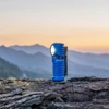 Blue Olight flashlight illuminating a mountain landscape at sunset.