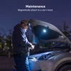 Man repairing car engine with a magnetic work light under the hood at night.